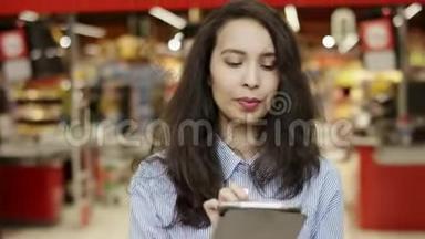 在超市里，一个迷人的黑发女孩在她的平板电脑上列出购物<strong>清单</strong>，列出要购买的<strong>物品</strong>，人们